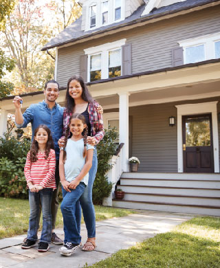 Young parents and two daughters in front of new home.